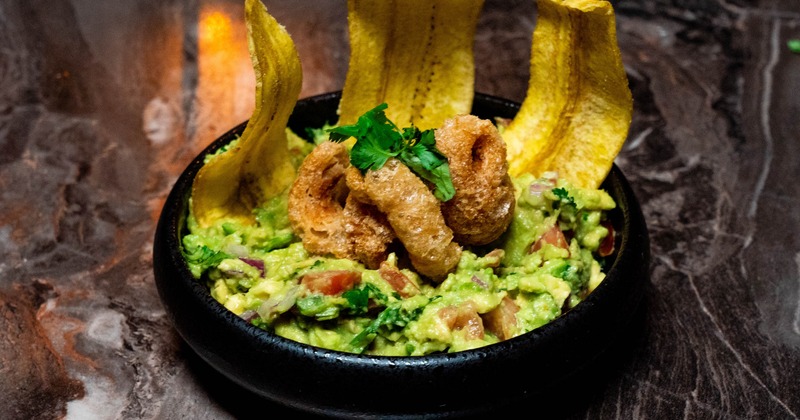 Guacamole garnished with deep-fried pork belly and fried plantain slices