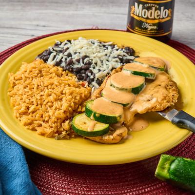 Grilled chicken topped with sauce and zucchini, served with rice, black beans, and cheese.