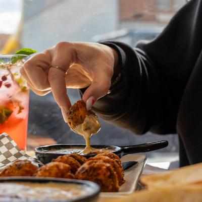 A hand dipping a tater tot into cheese dip.