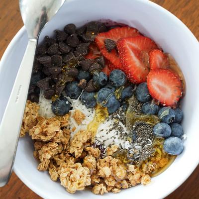 Breakfast bowl with granola, yoghurt, berries, chia seeds, chocolate chips, and honey.