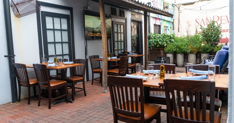 Outdoor dining area with wooden tables and chairs, surrounded by greenery and a colorful mural