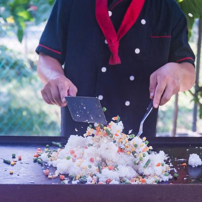 Chef cooking fried rice with vegetables on an outdoor griddle.