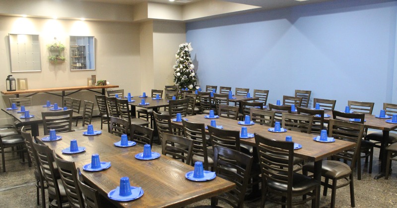 Wooden dining tables with dark chairs are set with blue party cups