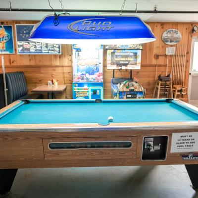 Pool table in a game room with booth seating and arcade games.