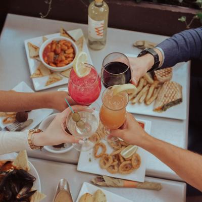 Toasting with cocktails over a table with served food, top view.