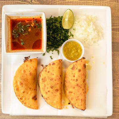 Birria tacos served with a side of dip with chopped onions, cilantro and lime wedge.