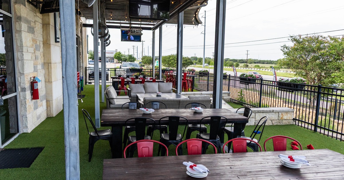 Outdoor dining area with tables, chairs, and gray sofas on artificial turf under a covered patio