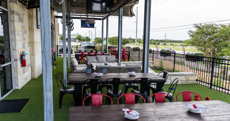 Outdoor dining area with tables, chairs, and gray sofas on artificial turf under a covered patio