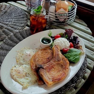 Pork chops and eggs served with a salad, dipping sauce, and a cocktail.