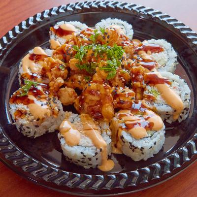 A plate of sushi rolls topped with spicy mayo, parsley, and sesame seeds.