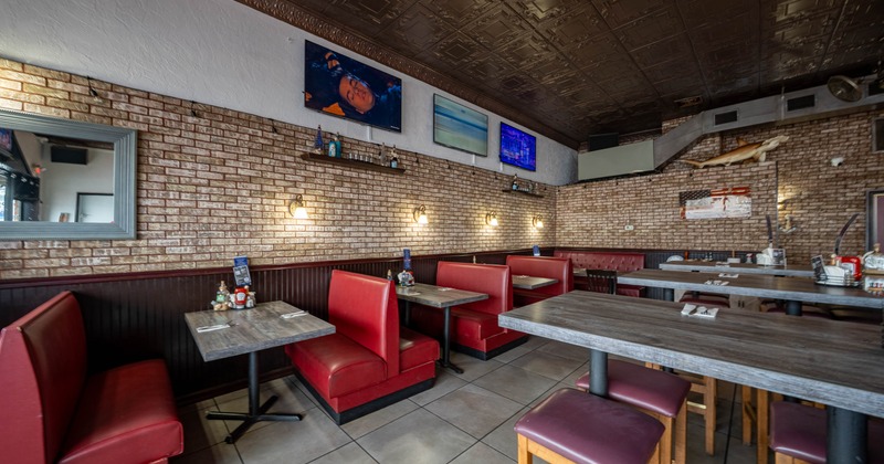 Interior of a diner with red booths, brick walls and mounted TVs.