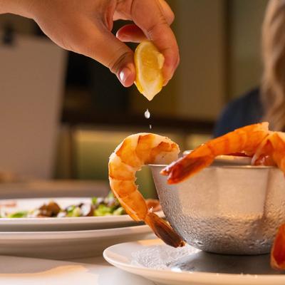 A hand squeezing lemon over a shrimp.