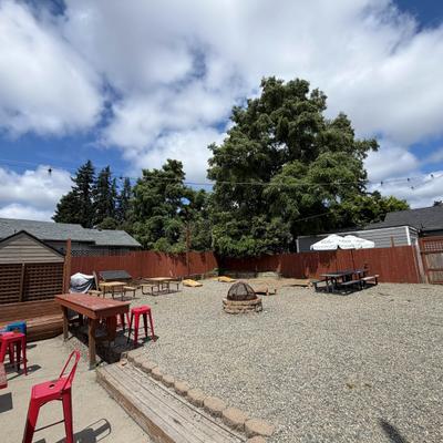 Gravel outdoor space featuring rustic wooden tables and red stools.