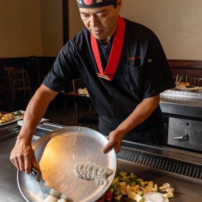 Teppanyaki chef in a red hat skillfully places seafood and vegetables on a hot grill.