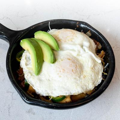 A dish with two fried eggs and sliced avocado on top, served in a skillet.