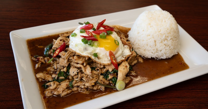 Stir fried chicken with fried egg, basil, and rice