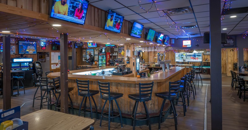 Interior of a bar with a wooden theme, featuring a U-shaped counter, bar stools, mounted TVs