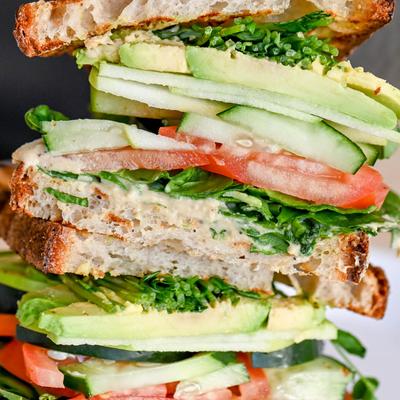 Sandwich with hummus, avocado, spinach, cucumber, tomato, apple, and pea shoots.