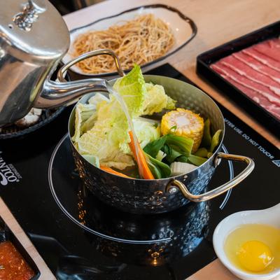 Broth being poured into a hot pot with vegetables and corn.
