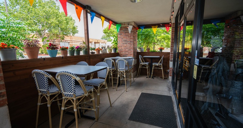 Exterior, patio with tables, chairs, colorful pennant flags, potted plants along the railing