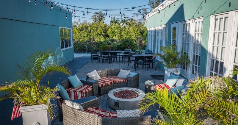 Outdoor patio area with wicker seating around a fire pit, potted palms, and string lights