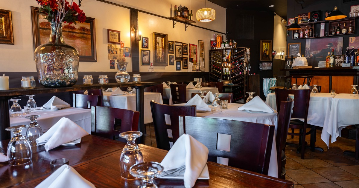 Warmly lit interior - white-tableclothed tables, floral décor, wall art, a wine rack, a stocked bar.