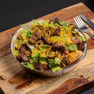 Bowl of steak nachos served on a wooden board.