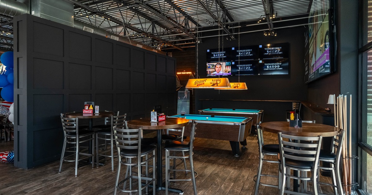 Interior, high-top tables, billiard table, black paneled wall, screens displaying sports scores