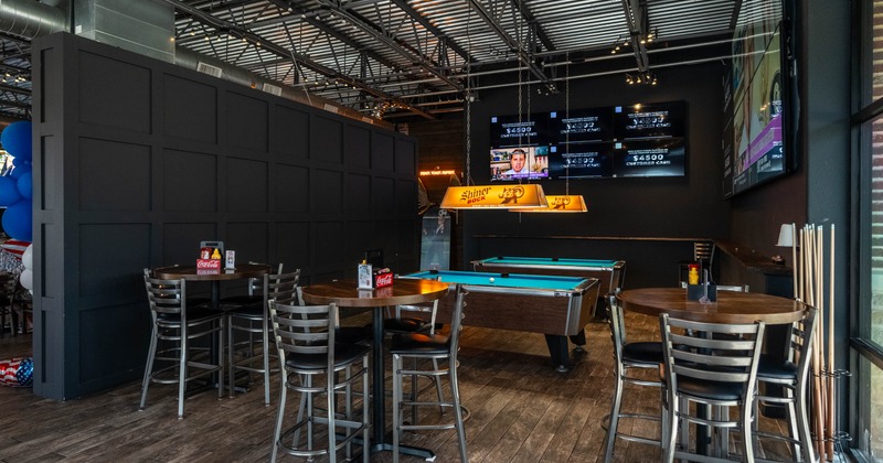 Interior, high-top tables, billiard table, black paneled wall, screens displaying sports scores