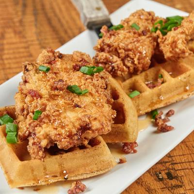 Fried chicken on waffles with syrup and green onions on a white plate