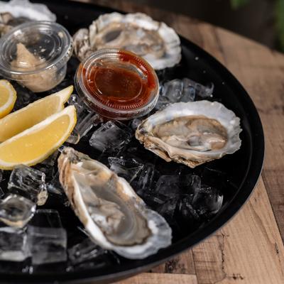 Fresh raw oysters served on ice with sauces and lemon wedges.