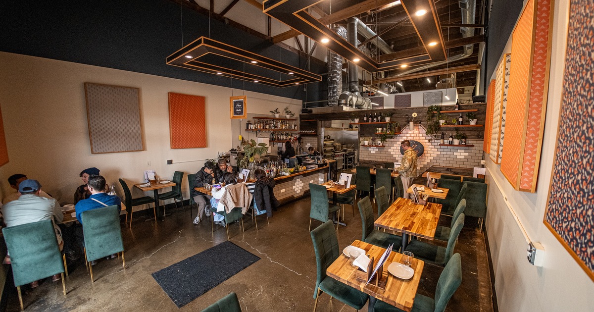Interior, wide view to restaurant diner area, tables, chairs, guests, bar behind