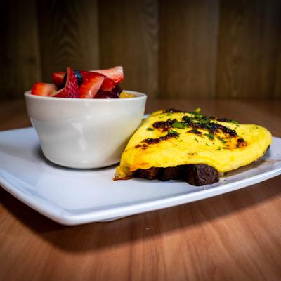 Omelet with steak pieces and sauce served with a bowl of mixed fruit.