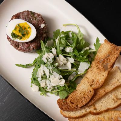 Beef tartare served with a soft-boiled egg, toast points, and arugula with Parmesan.