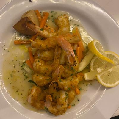 Breaded shrimp with sauteed vegetables in a light sauce, garnished with lemon slices.