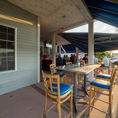 An outdoor restaurant patio features wooden tables, blue chairs, and a covered awning.