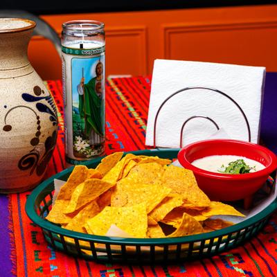 Queso dip with chips served on the table with a piece of pottery and a devotional candle.