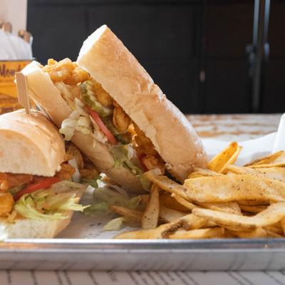 Buffalo shrimp sandwich served with fries on a metal tray.