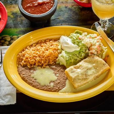Chimichanga covered in white sauce served with rice, beans, guacamole, and sour cream.