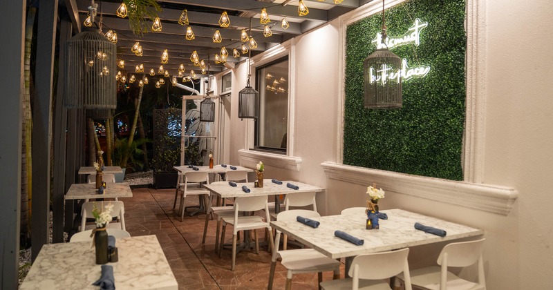 Outdoor dining area with marble tables, pendant lights and a neon sign on a green wall