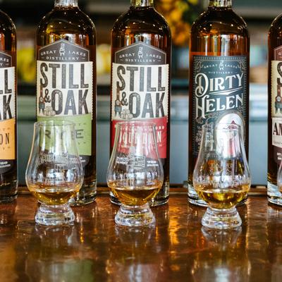 Still & Oak distillery liquor in bottles and filled glasses flight, front view.