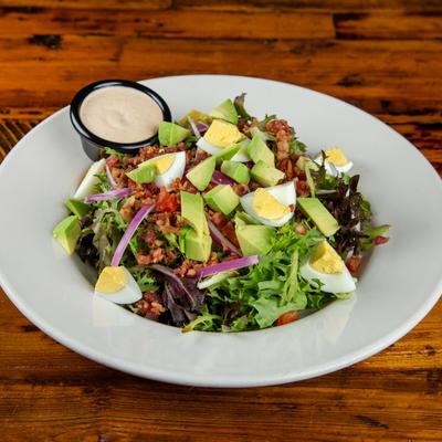 Cobb salad with avocado, tomato, bacon, hard-boiled egg, red onion and dressing.