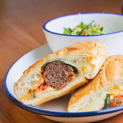 Meatball sub sandwich with melted cheese, tomato sauce, and a side salad.