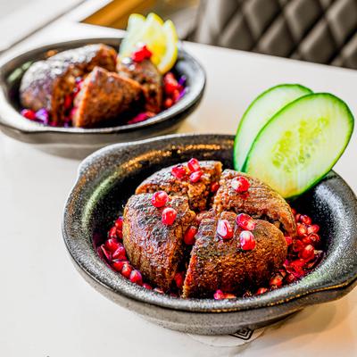 Two servings of Grilled kebbeh on a white table.