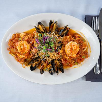 A seafood dish with shrimp, mussels, rice, garnished with microgreens.