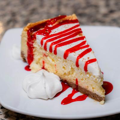 Mardi Gras Cheesecake drizzled with red sauce and garnished with whipped cream.