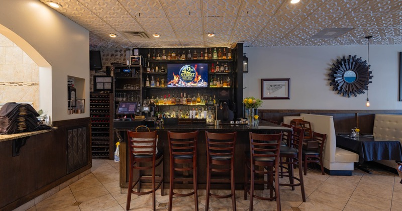 Interior of a bar and grill - a bar area, wooden chairs, shelves with bottles and a digital screen