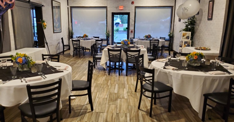 Round tables set with white tablecloths, black napkins, and floral centerpieces