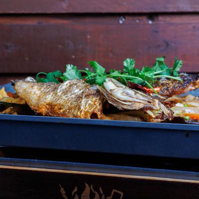Whole cooked fish with vegetables, dried chilies, and cilantro on a serving tray.