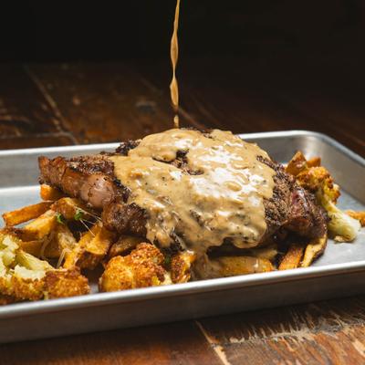 Creamy sauce being poured over ribeye steak.